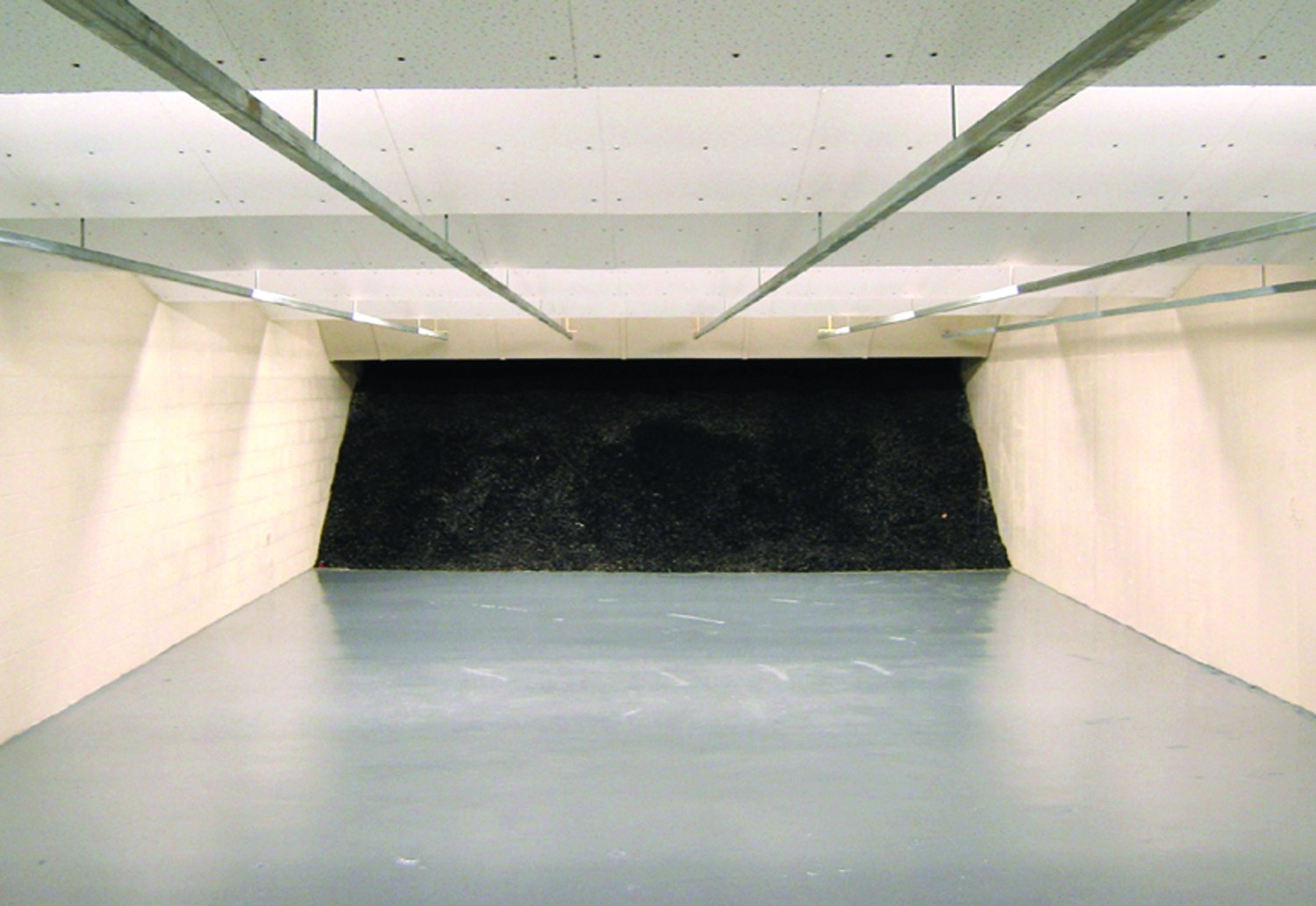 Indoor shooting range with white walls, overhead baffles, and a dark bullet trap at the back.