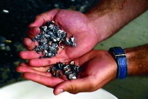 Hands hold small metal pieces over a surface, blue wristband visible.