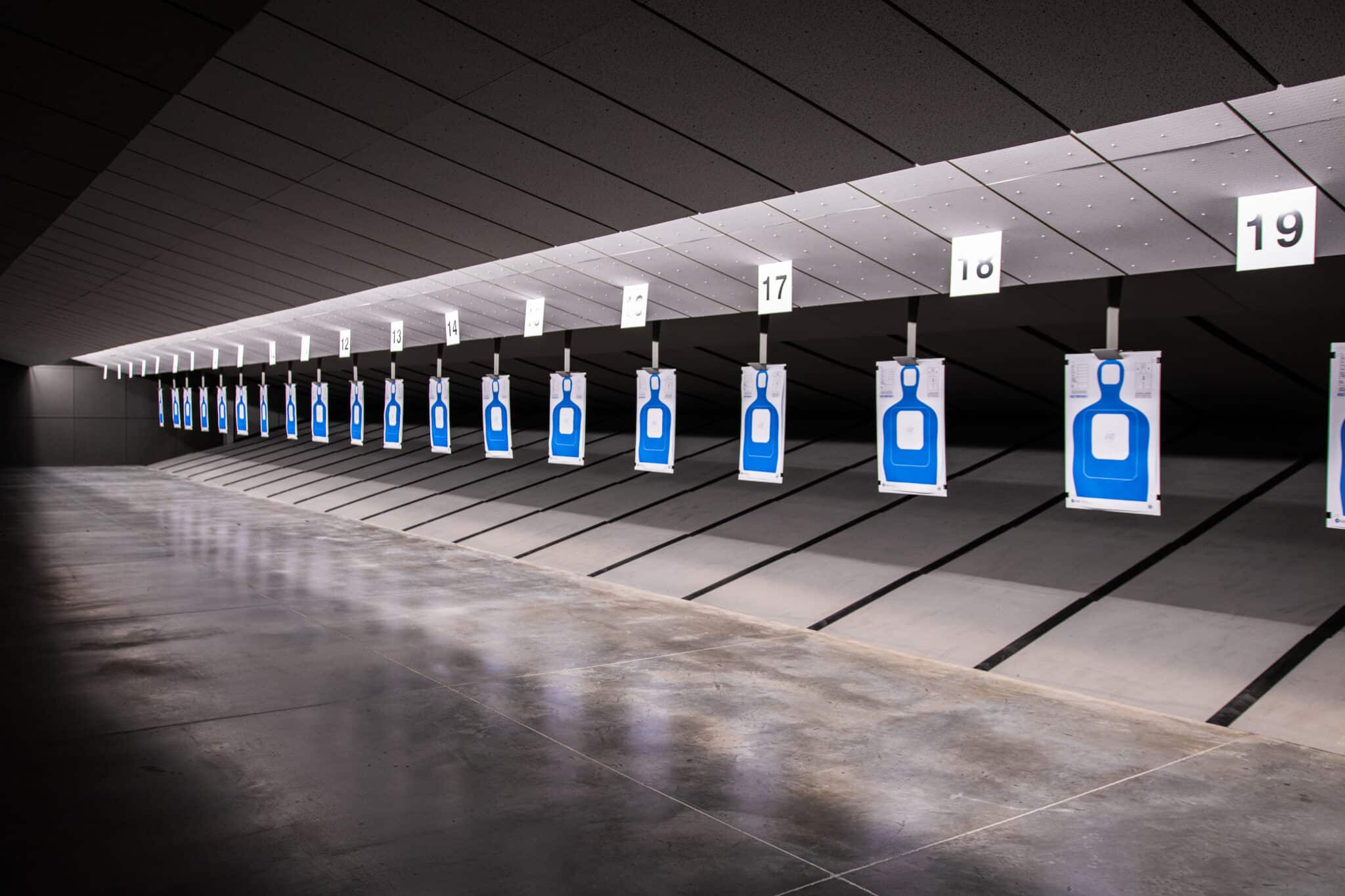 Numbered targets hang in a modern shooting range with a smooth, reflective floor.