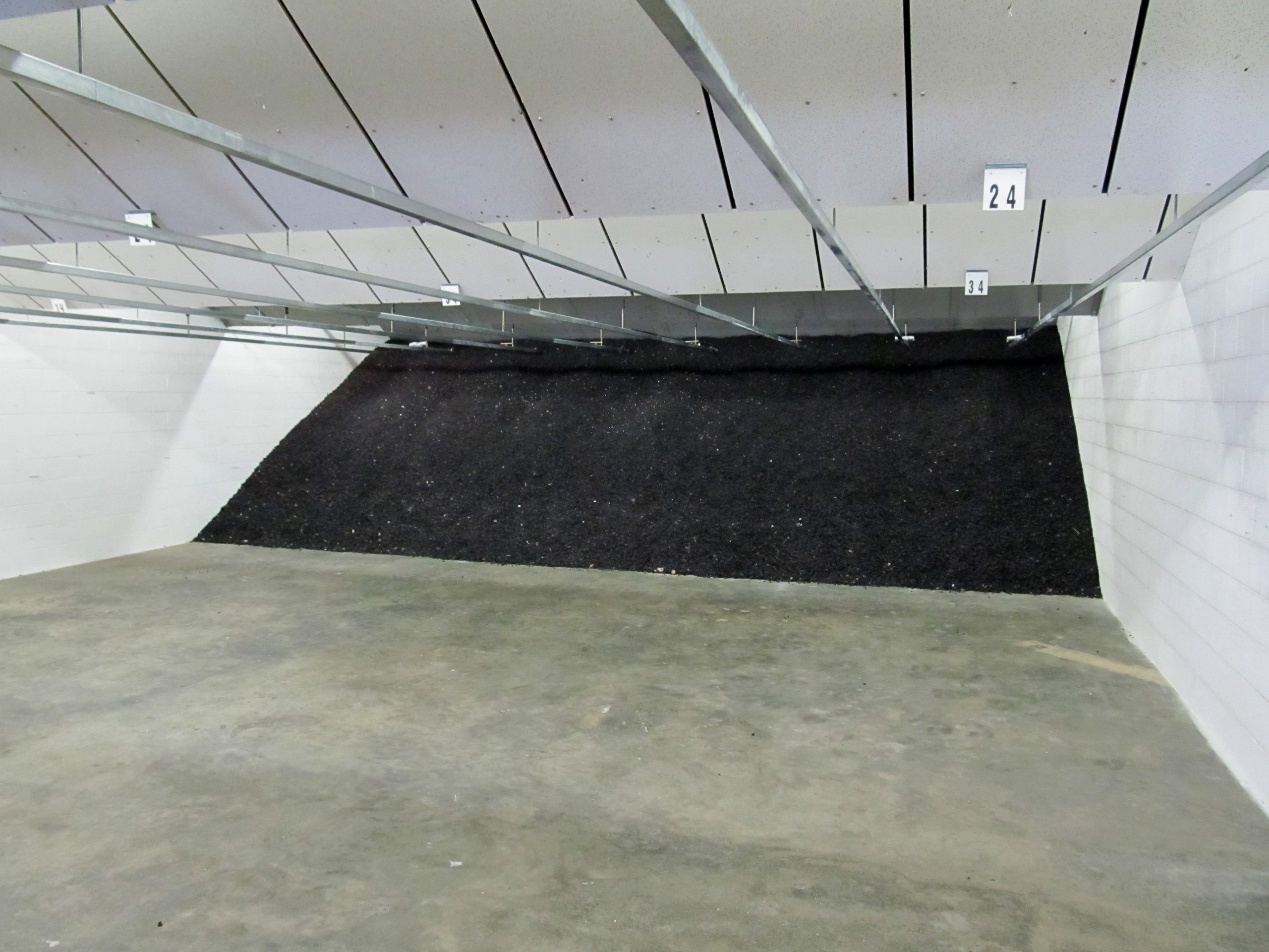 Indoor shooting range with a bullet trap at the back wall, concrete floor, and overhead target tracks.
