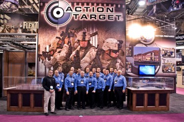 Group of people in blue shirts stand together at a display booth. Text: "ACTION TARGET."