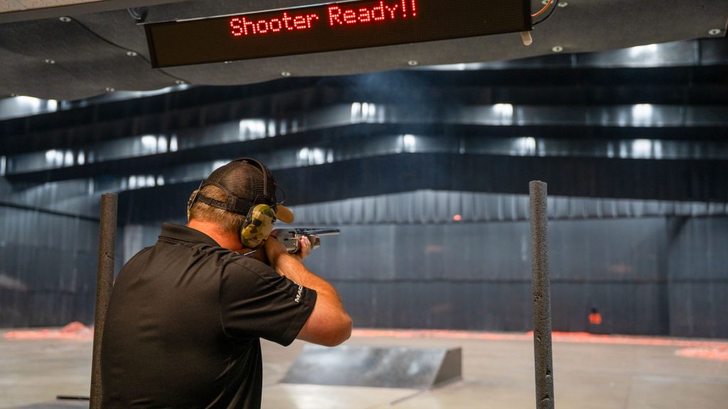 Man holding shotgun inside shotgun shooting range